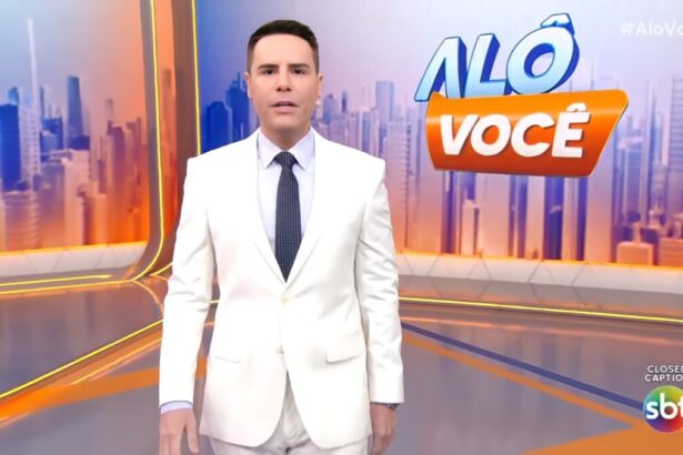 Luiz Bacci veste terno branco e com semblante assustado no cenário do Alô Você