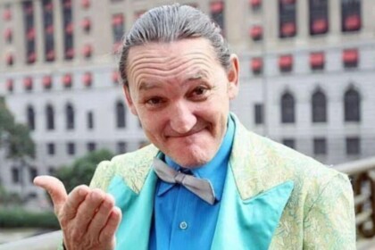 Marquito gesticulando com as mãos e sorridente nos bastidores de uma gravação na rua