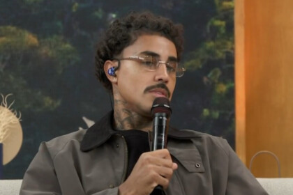 MC Livinho, com óculos e jaqueta escura, em trecho de participação no sofá do Encontro