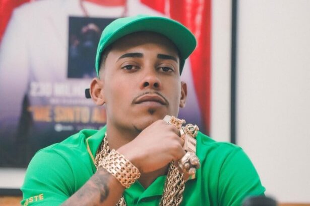 MC Poze do Rodo de camisa e boné verdes sentado e olhando para uma câmera com semblante sério