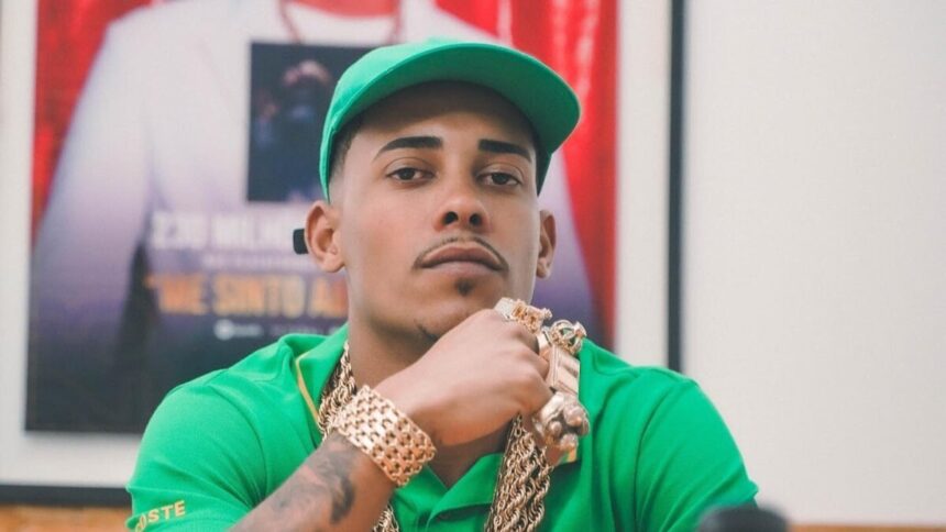 MC Poze do Rodo de camisa e boné verdes sentado e olhando para uma câmera com semblante sério