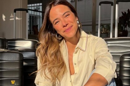 Miá Mello em foto posada, sorridente, com malas ao fundo