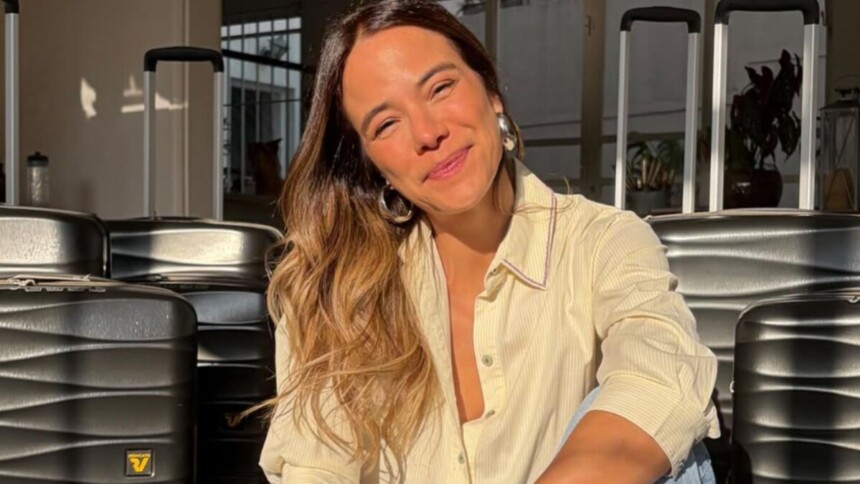 Miá Mello em foto posada, sorridente, com malas ao fundo
