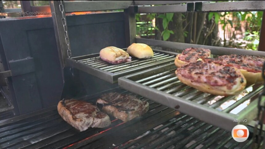 Chorizo com Pão de Alhobresa na grelha da churrasqueira de Thiago Oliveira no cenário do É de Casa. Fumaças saem da churrasqueira