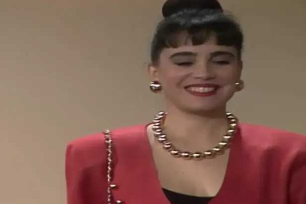 Maria do Carmos sorrindo de vestido e batom vermelhos em cena de Rainha da Sucata