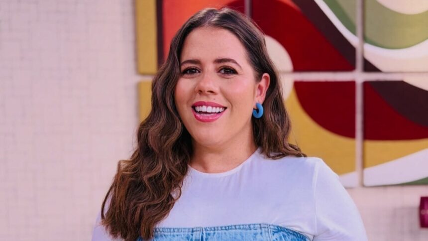 Tati Machado sorrindo em pé no cenário do Mais VocÊ