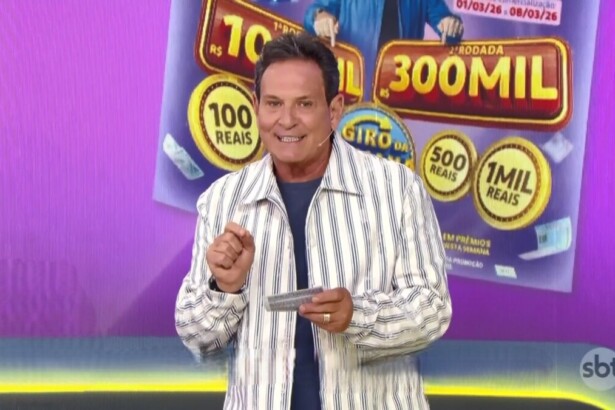 Luís Ricardo no centro do palco da Tele Sena Semanal edição 94. Ele está em frente ao telão que mostra o bilhete lilás