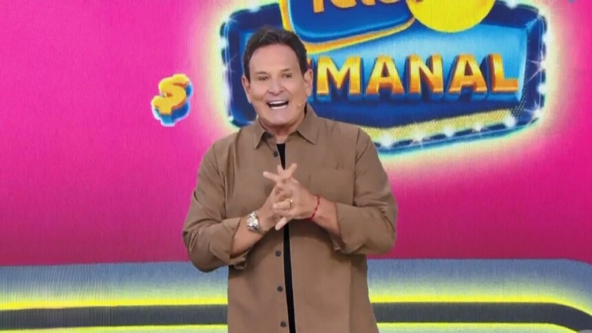 Luis Ricardo com as mãos unidas e sorridente em frente ao telão com o bilhete da Tele sena Semanal rosa edição 96