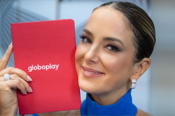 Ticiane Pinheiro sorrindo, segurando próximo ao rosto uma agenda vermelha com o logo do Globoplay