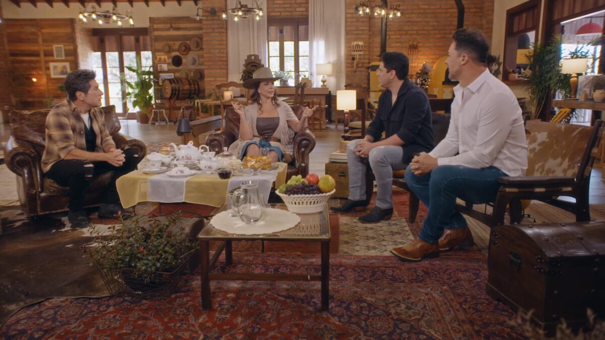 Sula Miranda fala enquanto Daniel e Hugo Pena & Gabriel olham para ela. Todos sentados numa sala da Fazenda
