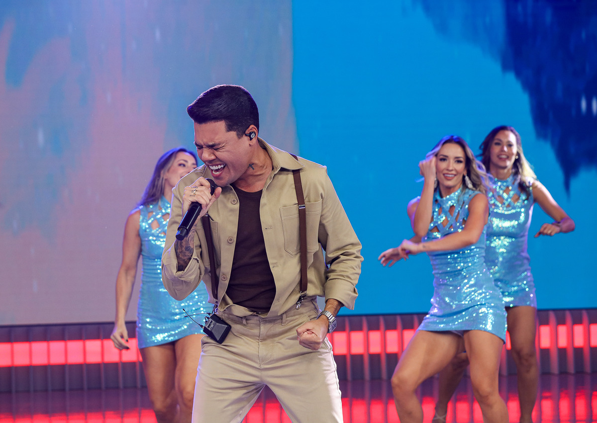 Felipe Araújo segura microfone e abre bema a boca em nota alta cantando no palco do Domingo Legal