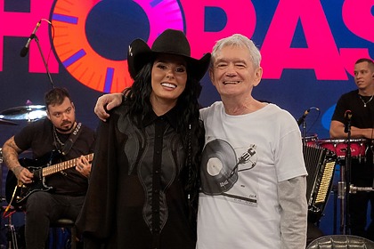Ana Castela e Serginho Groisman posando abraçados no cenário do Altas Horas