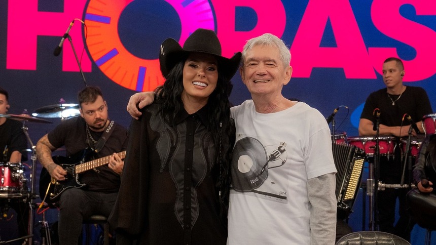 Ana Castela e Serginho Groisman posando abraçados no cenário do Altas Horas