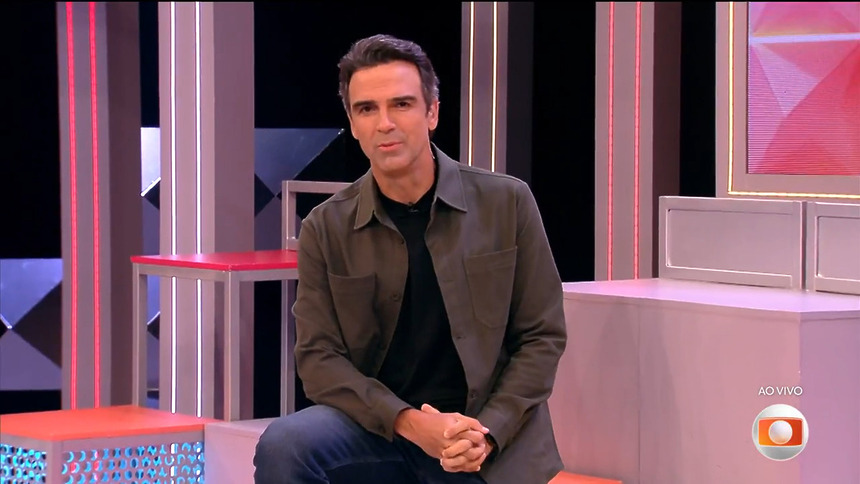 Tadeu Schmidt sentado nos blocos do cenário do programa anunciando as incrições do BBB 27