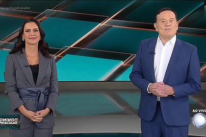 Camila Busnello ao lado de Cabrini. Os dois sorridentes em pé no cenário do Domingo Espetacular
