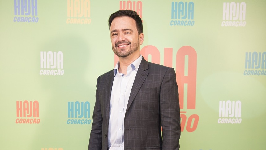 Daniel Ortiz autor da TV Globo de terno cinza em frente ao painel da estreia da novela Haja Coração