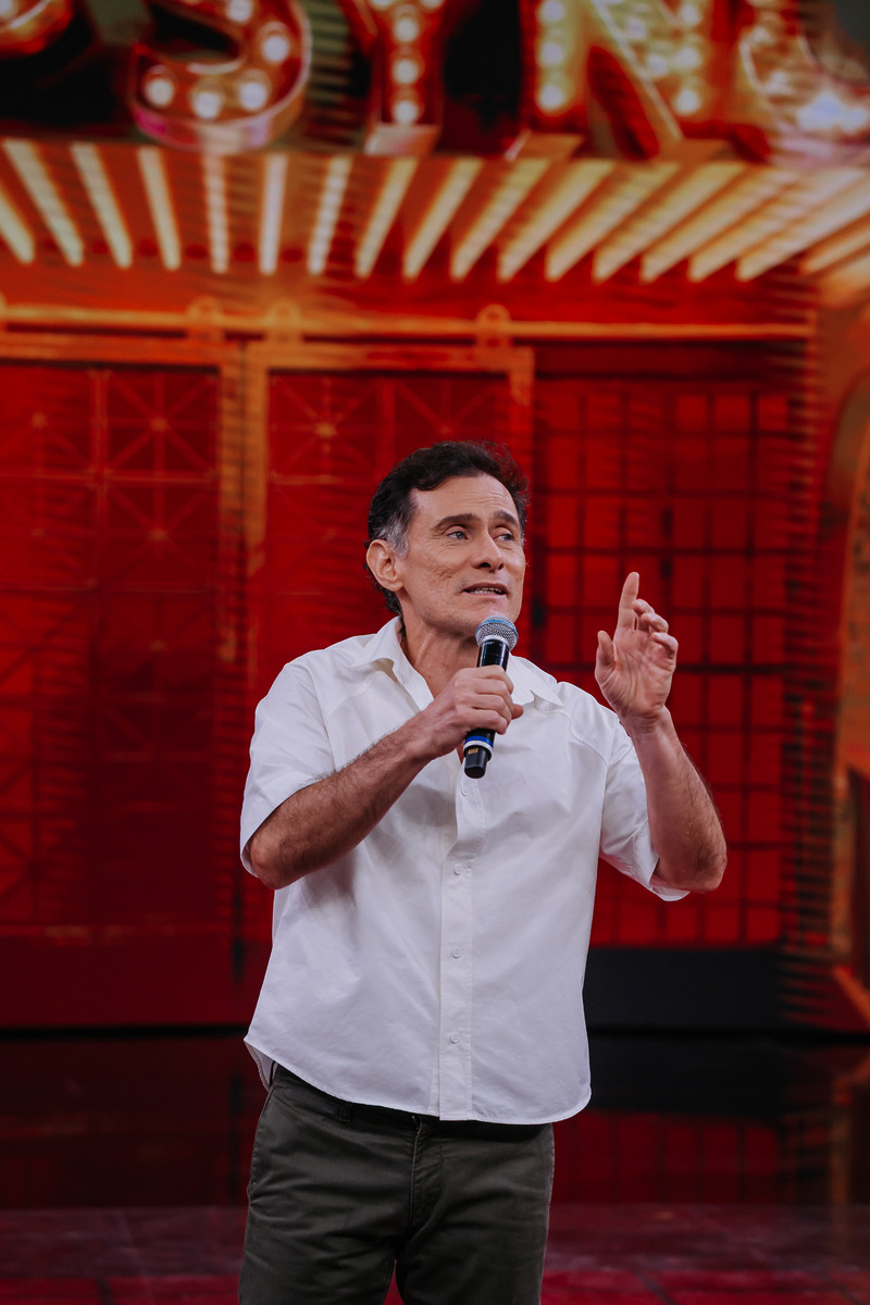 Enrique Diaz levanta o dedo enquanto conversa no palco do Domingão