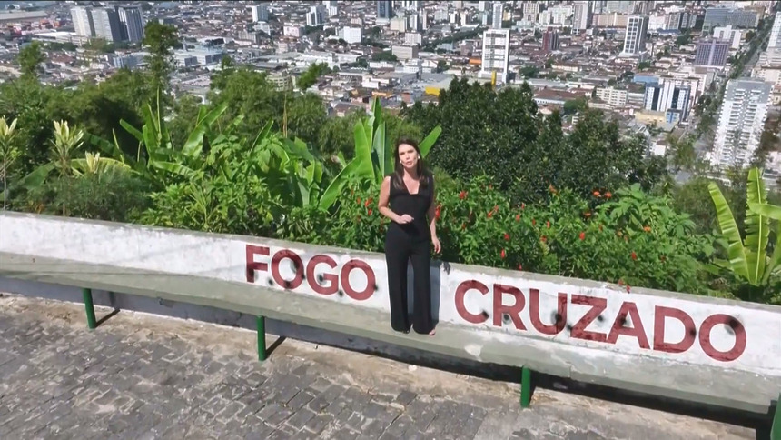Camila Busnello em cima de um morro, com uma frase digitalizada escrito Fogo Cruzado no muro em chamada do Domingo Espetacular
