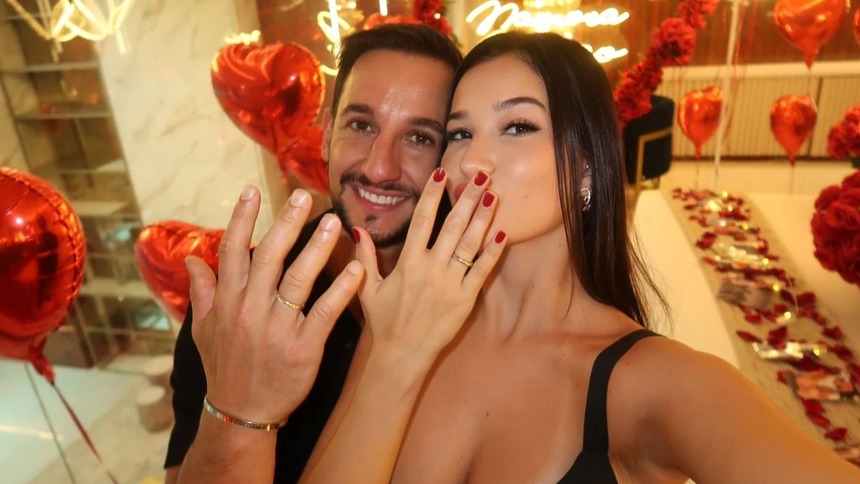 Duda Wendling e Luiz Mesquita posando juntos, mostrando o dedo de aliança