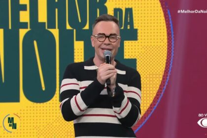Felipeh Campos sorridente segurando o microfone da Band em frente ao telão do Melhor da Noite