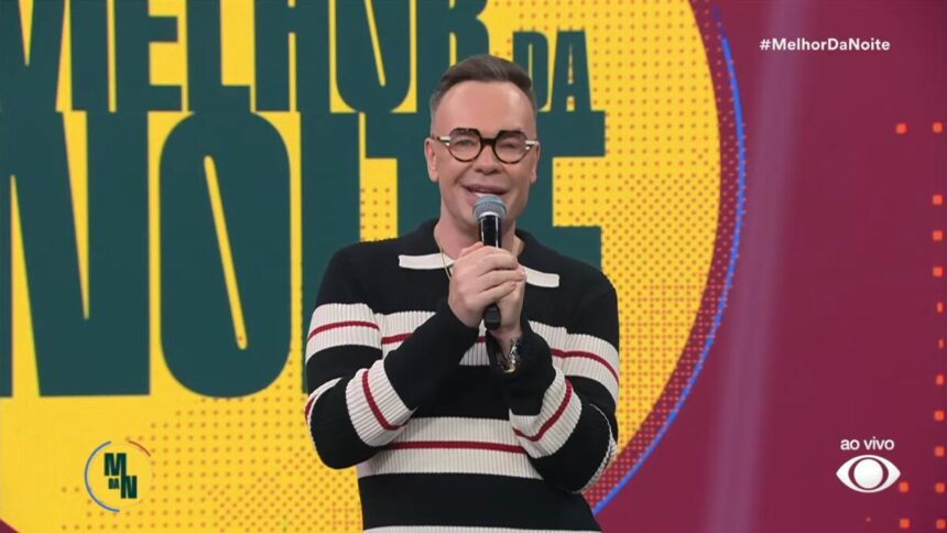 Felipeh Campos sorridente segurando o microfone da Band em frente ao telão do Melhor da Noite