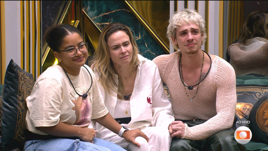 Milena, Ana Paula Renault e Juliano Floss sentados no sofá do BBB 26, chorando emocionados