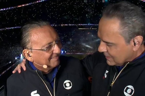 Galvão Bueno e Luis Roberto abraçados em um estádio, na cobertura de transmissão da TV Globo
