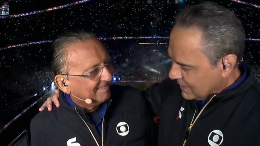 Galvão Bueno e Luis Roberto abraçados em um estádio, na cobertura de transmissão da TV Globo