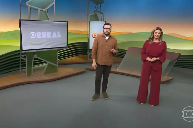 Pedro Málaga em pé ao lado de Cristina Vieira que veste um conjunto na cor vinho. Os dois estão sorridentes no cenário do Globo Rural