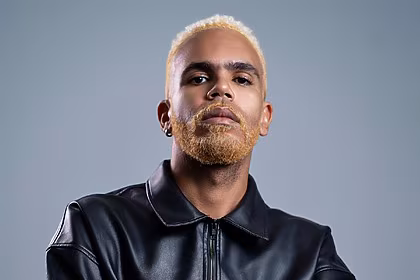 Hiran com casaco preto e olha sério em divulgação do novo álbum Imundo