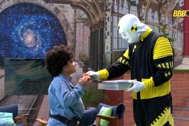 Milena recebendo a pulseira laranja do dummy após apertar o botão misterioso no BBB 26