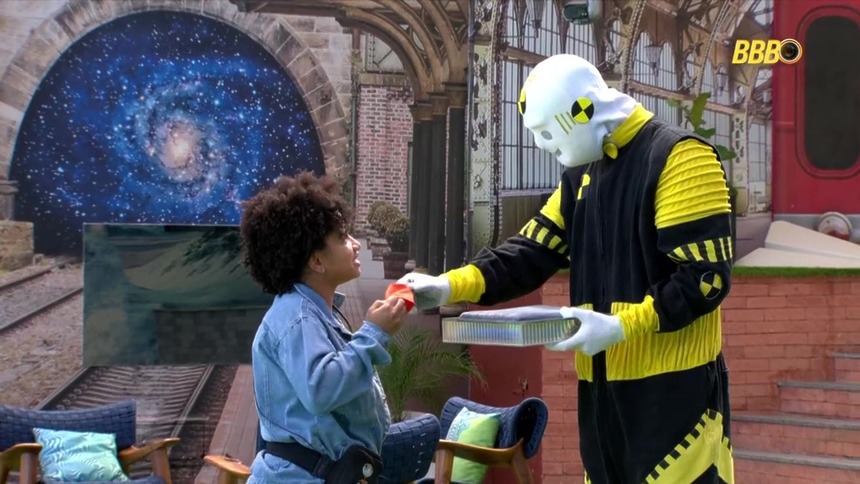 Milena recebendo a pulseira laranja do dummy após apertar o botão misterioso no BBB 26