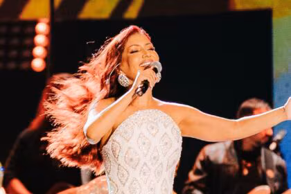 Priscila Senna de vestido branco com brilhantes dourados cantando em cima de um palco