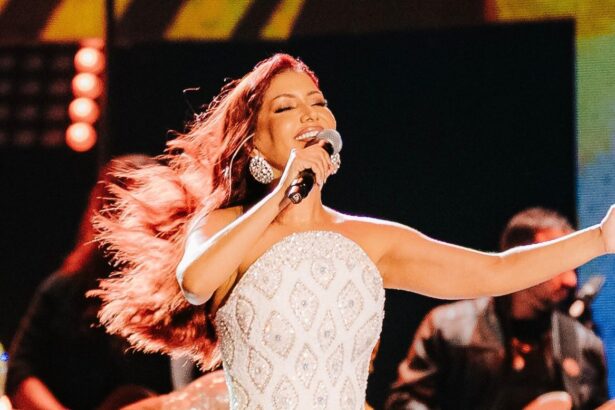 Priscila Senna de vestido branco com brilhantes dourados cantando em cima de um palco