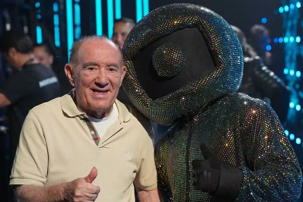 Renato Aragão fazendo o sinal de joia com o dedo, ao lado do mascote com o logo da Globo na cabeça, nos bastidores do Caldeirão
