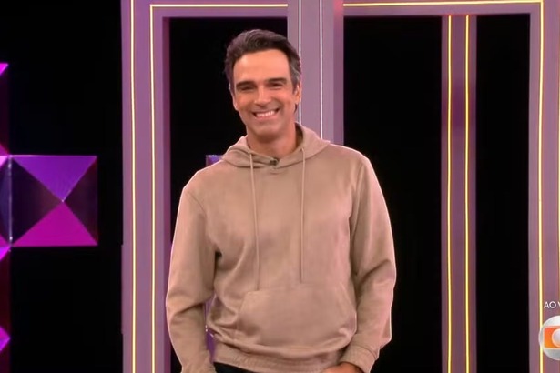 Tadeu Schmidt sorridente, de moletom, falando sobre a Prova do Anjo no BBB 26