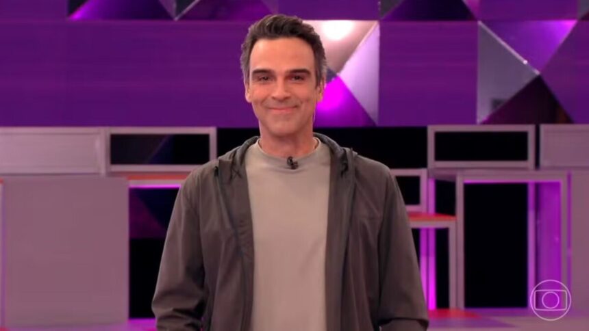 Tadeu Schmidt, sorriden no cenário do BBB 26, explicando a dinâmica da semana