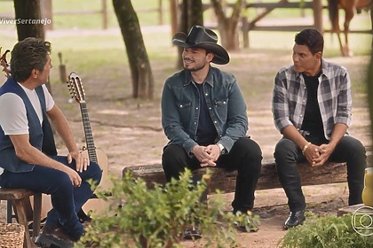 Carreiro & Capataz sentados no banco de madeira olhando para Daniel no Viver Sertanejo