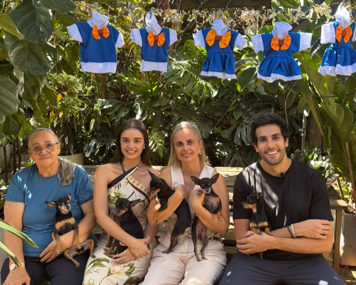 Dona Darci, com os cachorros, a Filha a Neta, ao lado do apresentador Julinho Casares sentados em um banco na reportagem do Hoje Em Dia