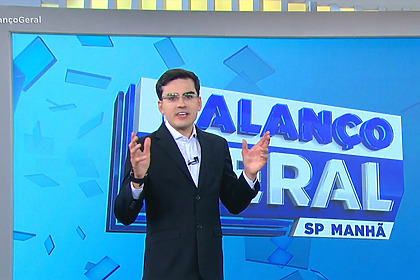 Dudu Camargo com os braços levantados em frente ao telão do Balanço Geral Manhã na RECORD