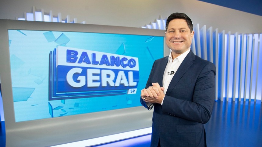 Eleandro Passaia sorridente, em frente ao telão, no cenário do Balanço Geral
