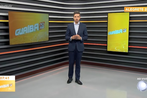 Leonardo Lara apresentando o Guaíba no Ar. Ele está de terno preto no novo cenário da RECORD Guaíba que tem piso branco, paredes em tons escuros, com linhas de LED amarelo e laranja