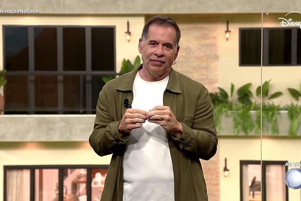 Leandro Hassum de blusa branca e casaco verde, gesticulando, no glass de estúdio da Casa do Patrão
