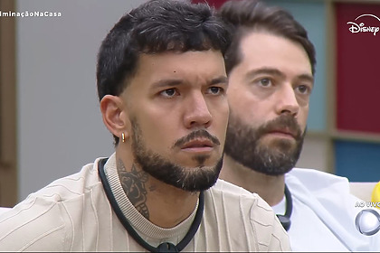 Luis Fellipe sentado no sofá da Casa Do Patrão atento ao telão onde Leandro Hassum discursa para o eliminado