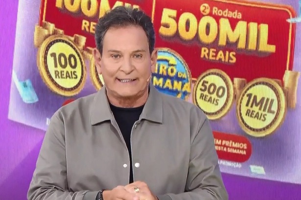 Luis Ricardo em pé na frente do telão com o bilhete da Tele Sena Semanal edição 104