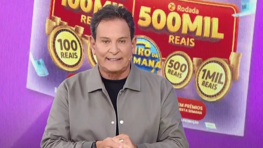 Luis Ricardo em pé na frente do telão com o bilhete da Tele Sena Semanal edição 104