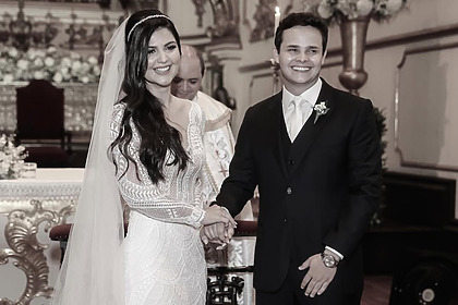 Paula Aires ao lado de Matheus Aleixo no altar de uma igreja católica. Eles se dão as mãos no casamento