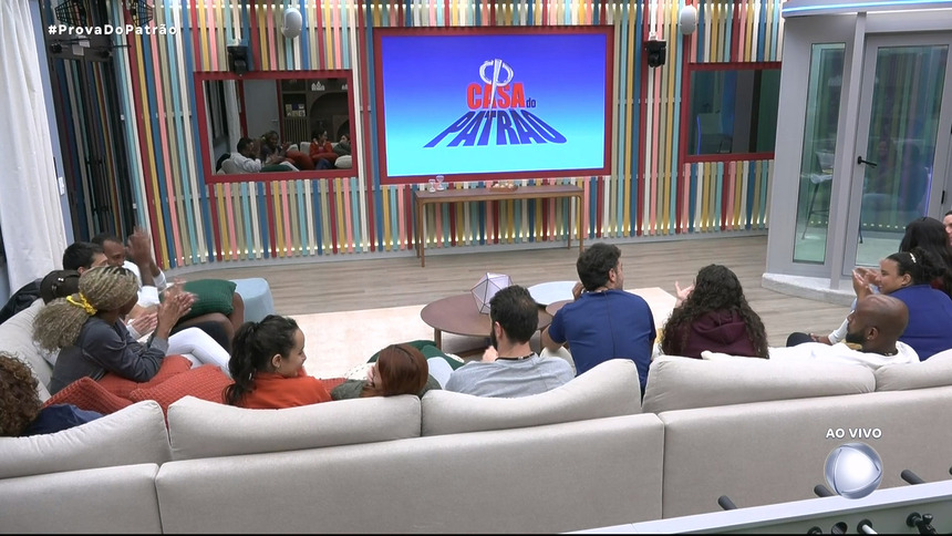 Participantes da Casa do Patrão olham para o telão após descobrirem como vai funcionar as novas regras do reality show