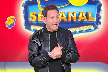 Luis Ricardo caminha no cenário do sorteio da Tele Sena Semanal. O cenário está com artes gráficas na cor vermelha da edição 105