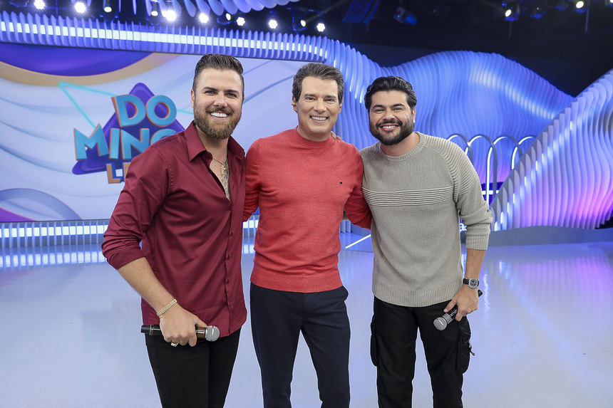 Celso Portiolli abraça Zé Neto E Cristiano no palco do Domingo Legal, ambos estão bem felizes e sorridentes